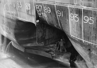 An unidentified officer inspects HMNZS Leander's extensive torpedo damage, Calliope Drydock 1943.