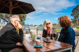 Local dining outside at Torpedo Bay cafe with ocean behind them